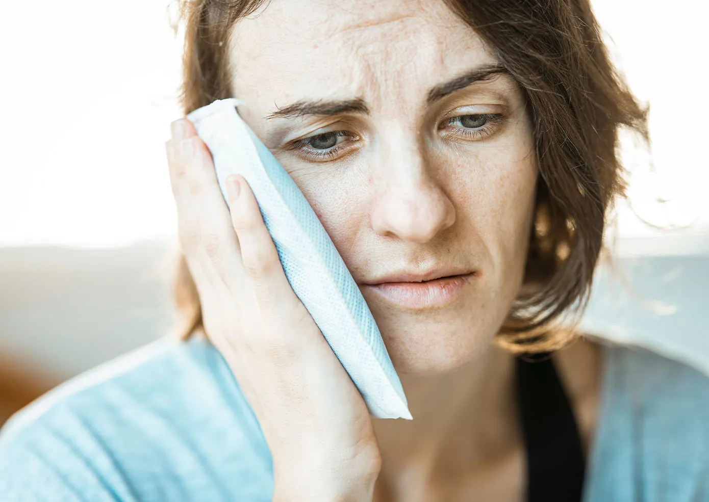 A woman holding an ice pack to her cheek with a pained look on her face